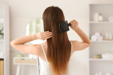Fototapeta premium Beautiful young woman brushing her hair in bathroom at home, back view