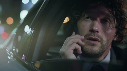 Young businessman looking out car window and talking on smartphone during night city ride with blurred street lights in background - Powered by Adobe