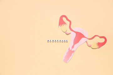 Word MENOPAUSE with paper uterus on beige background