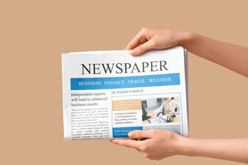 Female hands with newspaper on beige background