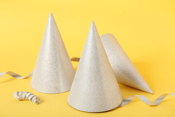 Beautiful party hats and serpentine on yellow background