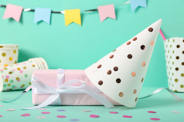 Party hat, gift box and decor on color background