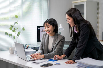 women are sitting at a desk, one of them is typing on a laptop