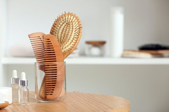 Glass with hair brush, combs and cosmetic products on wooden table in room