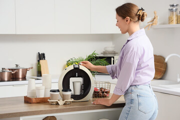 Pretty young woman using modern coffee machine in kitchen