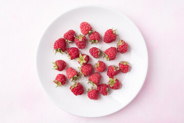 Top view of fresh ripe raspberry with leaf in white plate on pink background, Summer fruit