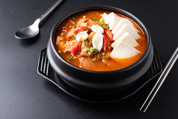 Korean food (Kimchi Jjigae), Kimchi soup with tofu, pork, scallion and chili in Korean stone bowl on black background