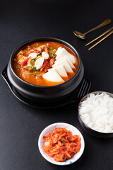 Korean food (Kimchi Jjigae), Kimchi soup with tofu, pork, scallion and chili in Korean stone bowl eating with cooked rice and kimchi cabbage on black background