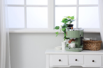 Modern coffee machine with cups and houseplant on table near window