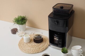 Modern coffee machine and cups of espresso on table near beige wall