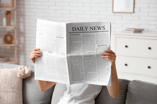 Woman reading newspaper on sofa at home