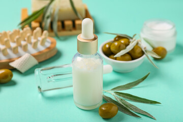 Bottles of natural essential oil, massage brush and green olives on color background