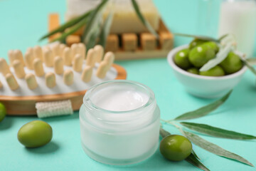 Jar of natural cream, massage brush and green olives on color background