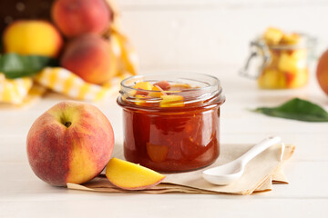 Glass jar of tasty peach jam and fresh fruits on light wooden table