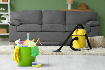 Bucket with cleaning supplies and vacuum cleaner on floor in living room