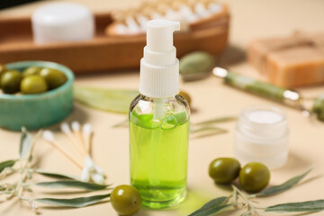 Bottle of natural cosmetic product, spa accessories and green olives on color background