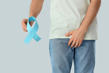 Young man with blue ribbon on light background, closeup. Prostate cancer awareness concept