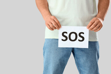 Young man holding paper with word SOS on light background, closeup. Prostate cancer awareness...