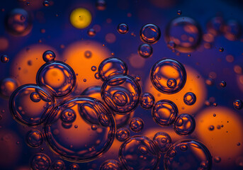Close-up of numerous translucent bubbles, reflecting orange light against a dark blue background, creating a visually striking abstract pattern.