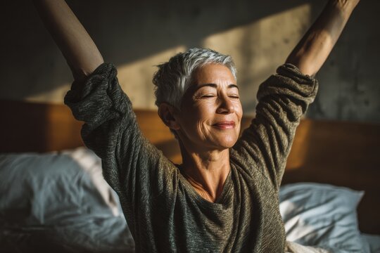 Joyful older woman with gray hair stretching in bed enjoying the sun at home in a hotel or camping - Powered by Adobe