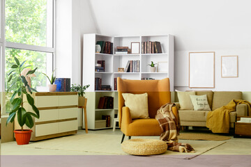 Obraz premium Interior of stylish living room with brown armchair, wicker pouf and bookshelf