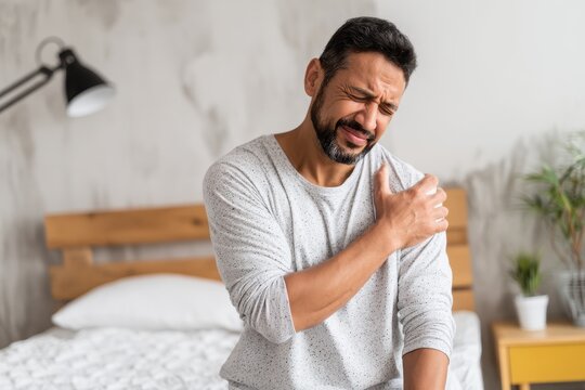 Young Hispanic man with a shoulder injury sitting on a bed