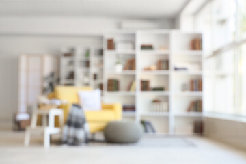 Blurred view of stylish living room with yellow armchair, pouf and bookshelf
