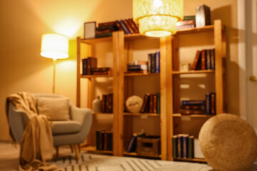 Interior of stylish living room with grey armchair, glowing lamps and bookshelves at evening