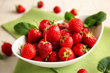 Bowl with sweet ripe strawberries and mint leaves on white tile background, closeup