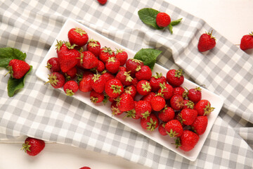 Plate with sweet ripe strawberries and mint leaves on white wooden background