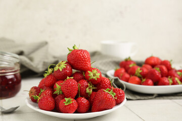 Plates with sweet ripe strawberries on white tile table