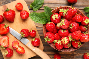 Bowl and cutting board with sweet ripe strawberries on wooden background
