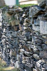 A rock wall of style grey rocks of various sizes. The irregular style natural stones stacked makes a rough textured barrier wall. The archaeological stone structure is rough and built without cement. 