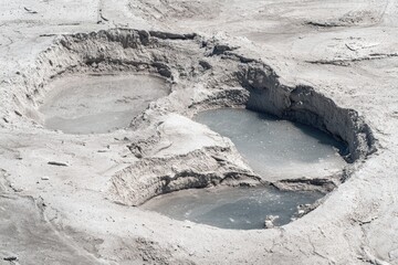 Three steaming pools in a light gray, cratered landscape