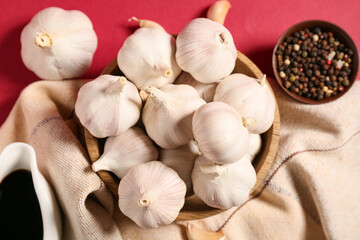 Wooden bowl with fresh garlics and gravy boat of soy sauce on red background