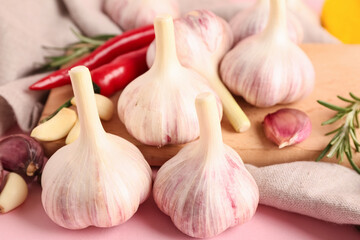 Wooden board with fresh garlics, rosemary and chili peppers on pink background, closeup