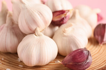 Wooden board with fresh garlics on pink background, closeup