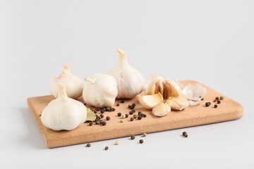 Wooden board with fresh garlics and peppercorns on grey background