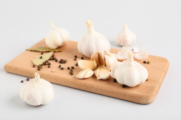 Wooden board with fresh garlics, peppercorns and bay leaves on grey background