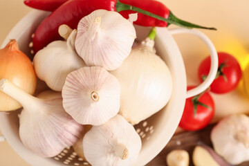Colander with fresh garlics, onions and chili peppers on beige background