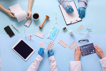 Doctors with patient card, medicine and clipboard working at blue table, top view