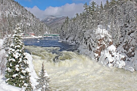 Winter waterfall scene with snow-covered forest and mountains