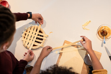 African American father and daughter weaving lattice over filling in pie dish on kitchen counter
