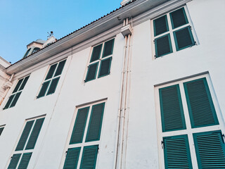 Fatahillah Museum or Jakarta History Museum facade in Kota Tua with colonial architecture, green wooden shutters, and white walls under blue sky