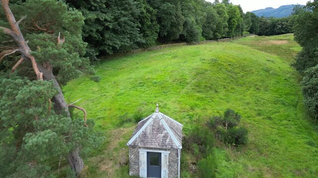 Aerial view of Earthquake House in Comrie, Scotland, surrounded by lush grassland and dense woodland
