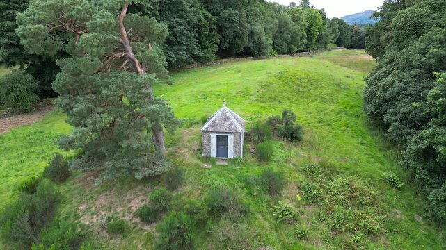 Aerial view of Earthquake House in Comrie, Scotland, surrounded by lush grassland and dense woodland