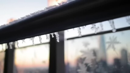 Frost-covered railing with icicles at sunset, city skyline in the background, serene winter scene - Powered by Adobe