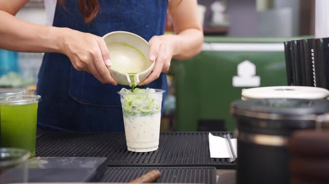 Small business entrepreneur coffee shop cafe and restaurant. Asian woman barista preparing iced matcha green tea latte on bar counter. Waitress working part time job serving beverage drink to customer