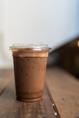 A glass with iced chocolate milk on transparent cup glass on wood table.