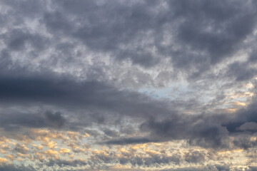 Layered clouds with soft sunlight breaking through, casting warm tones against a predominantly grey sky